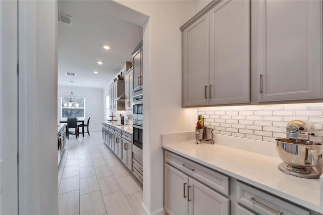 kitchen with tasteful backsplash, visible vents, oven, light countertops, and gray cabinetry