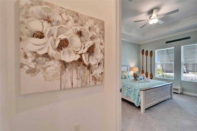 carpeted bedroom with ceiling fan, a tray ceiling, baseboards, and crown molding