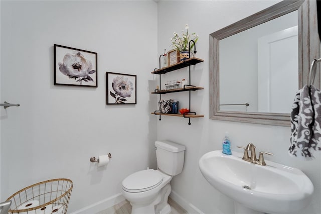 half bath featuring toilet, baseboards, and a sink
