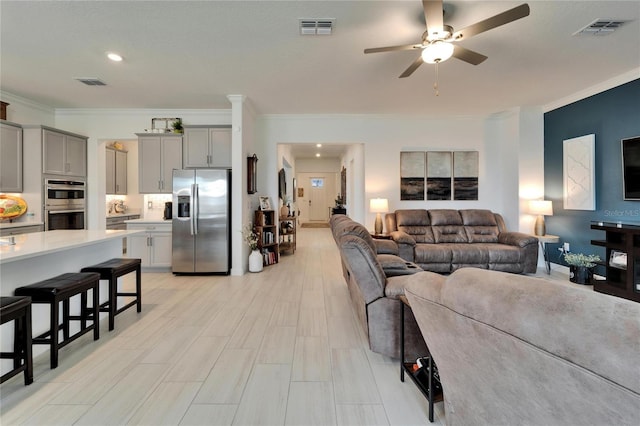 living area with visible vents, a ceiling fan, and ornamental molding