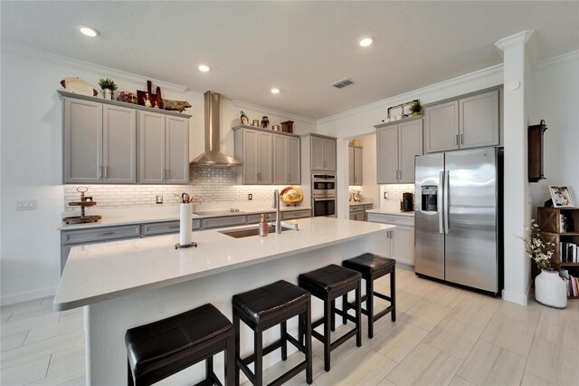 kitchen featuring stainless steel appliances, gray cabinets, visible vents, a sink, and wall chimney range hood