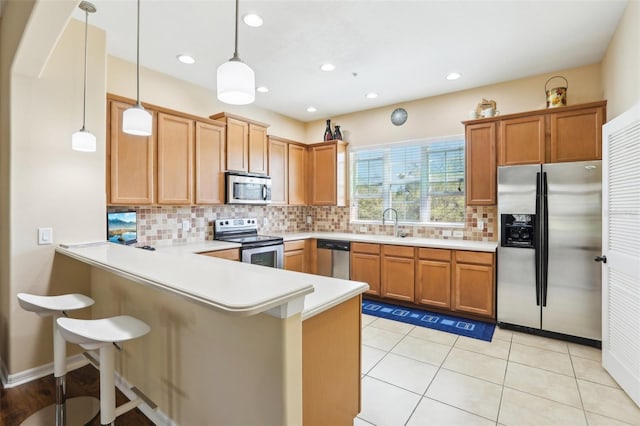 kitchen with a breakfast bar, a peninsula, light countertops, decorative backsplash, and stainless steel appliances