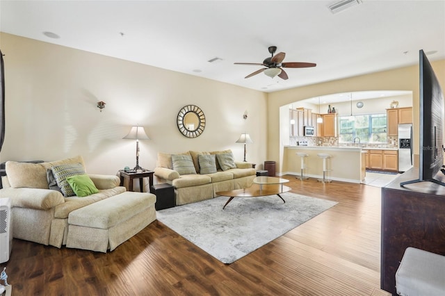 living room featuring arched walkways, visible vents, a ceiling fan, and wood finished floors