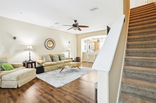living room featuring ceiling fan, visible vents, stairway, wood finished floors, and baseboards