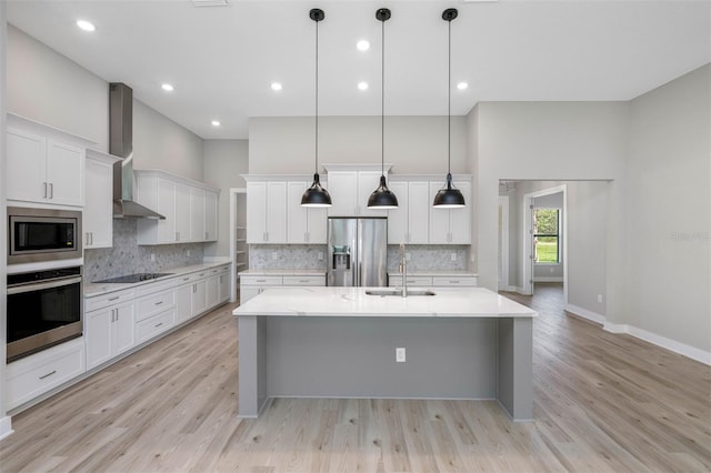 kitchen featuring a towering ceiling, a spacious island, wall chimney exhaust hood, appliances with stainless steel finishes, and a sink