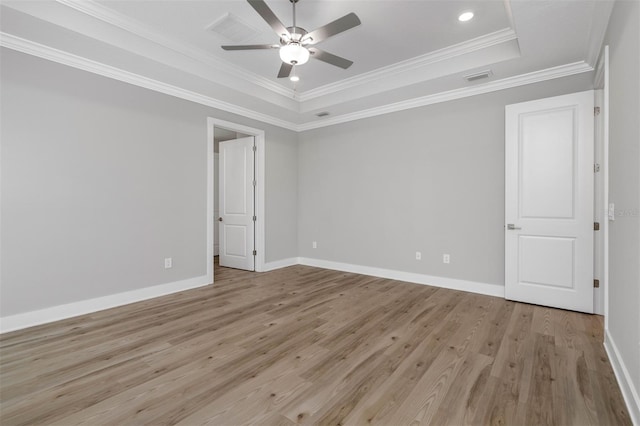 unfurnished room featuring ornamental molding, a tray ceiling, light wood-style flooring, and baseboards