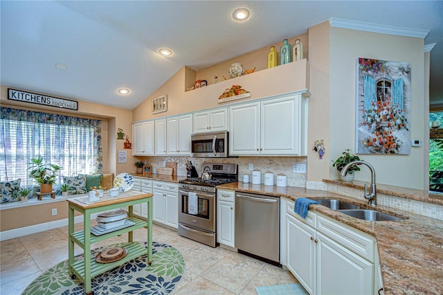 kitchen featuring tasteful backsplash, white cabinets, light stone countertops, stainless steel appliances, and a sink