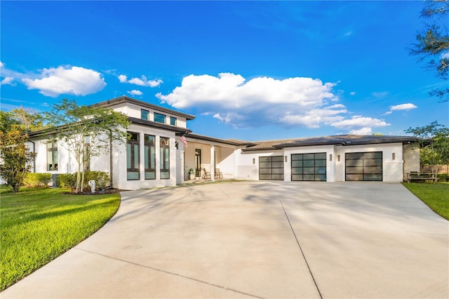 prairie-style house with a garage, driveway, a front lawn, and stucco siding