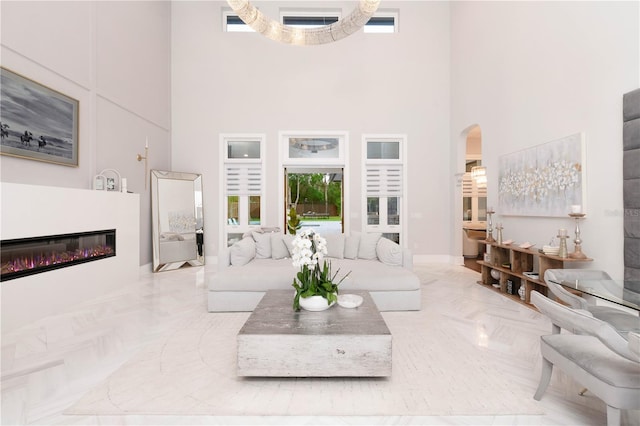 living room with arched walkways, a glass covered fireplace, and a high ceiling