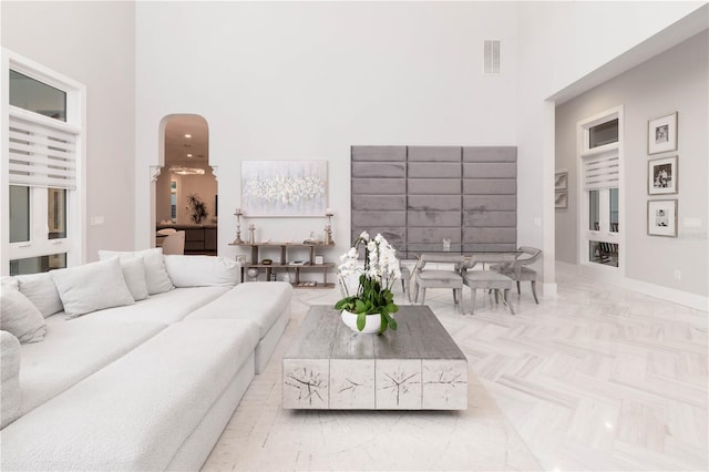 living room featuring arched walkways, visible vents, a towering ceiling, and baseboards