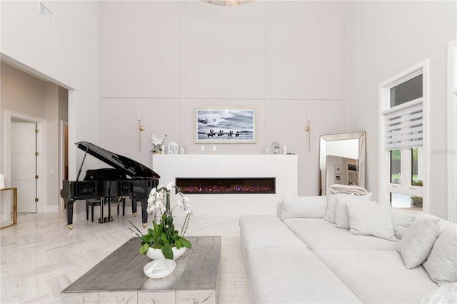 living room featuring a high ceiling, visible vents, and a glass covered fireplace