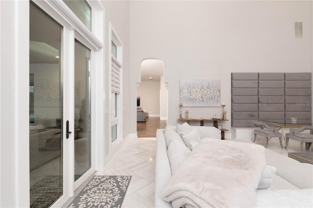 living area featuring baseboards, a high ceiling, visible vents, and arched walkways