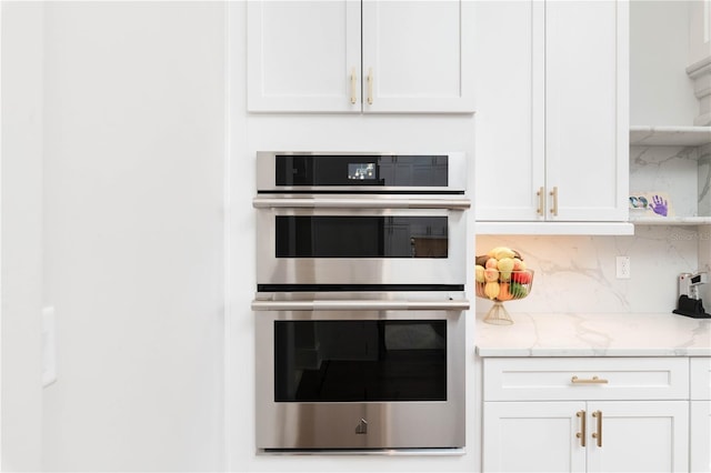 kitchen with light stone countertops, tasteful backsplash, white cabinets, and stainless steel double oven