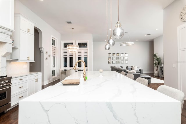 kitchen featuring a spacious island, dark wood-type flooring, white cabinetry, a sink, and light stone countertops