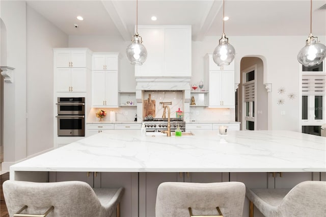 kitchen featuring a spacious island, double oven, tasteful backsplash, and beamed ceiling