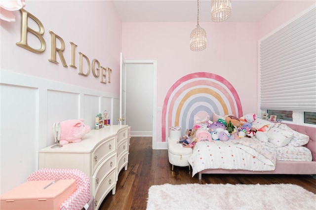 bedroom featuring a decorative wall, dark wood finished floors, a notable chandelier, and wainscoting