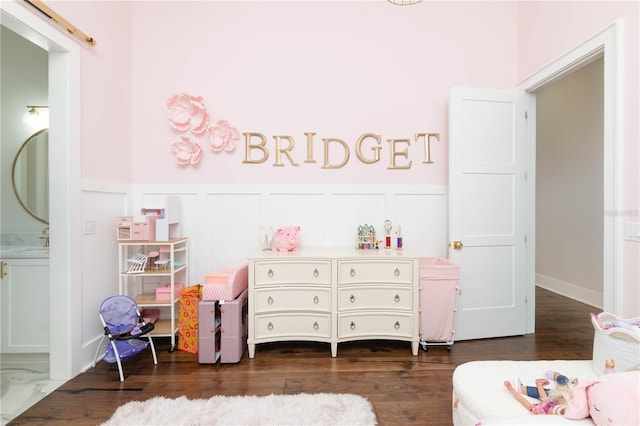 playroom featuring dark wood-style floors, wainscoting, a sink, and a decorative wall