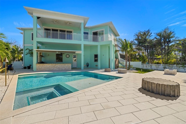 back of house with an in ground hot tub, a patio, a balcony, and a ceiling fan