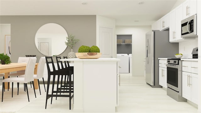 kitchen featuring light countertops, appliances with stainless steel finishes, white cabinetry, light wood-type flooring, and washer and dryer