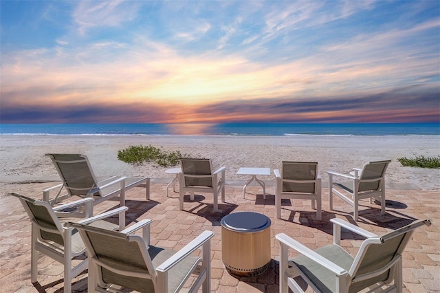 patio terrace at dusk featuring a beach view and a water view