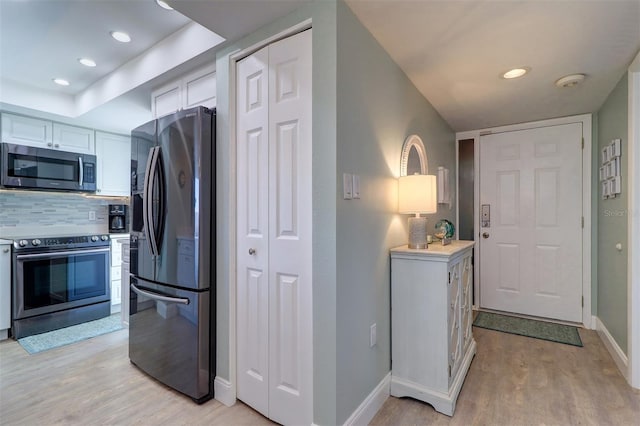 kitchen with baseboards, light wood finished floors, decorative backsplash, white cabinets, and appliances with stainless steel finishes