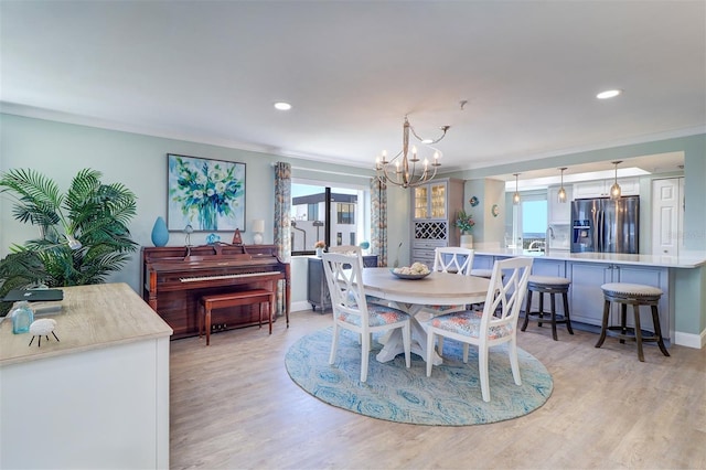 dining space with a wealth of natural light, crown molding, light wood-style floors, and an inviting chandelier