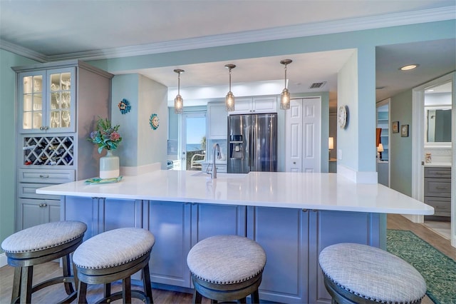 kitchen with visible vents, stainless steel fridge, a breakfast bar area, and ornamental molding