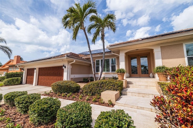 view of front of property with french doors, solar panels, stucco siding, a garage, and driveway