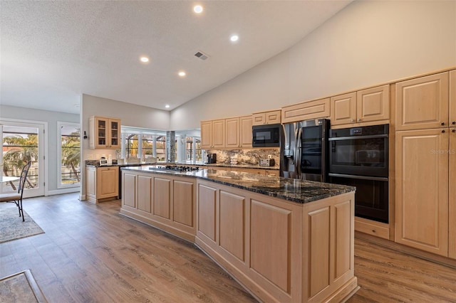 kitchen featuring a center island, glass insert cabinets, light wood-style floors, light brown cabinets, and black appliances