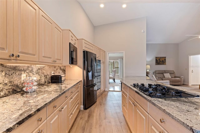 kitchen with open floor plan, black appliances, light stone counters, and backsplash