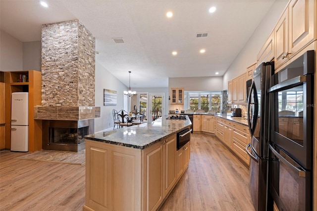 kitchen featuring visible vents, dark stone counters, light wood-style floors, black appliances, and light brown cabinets