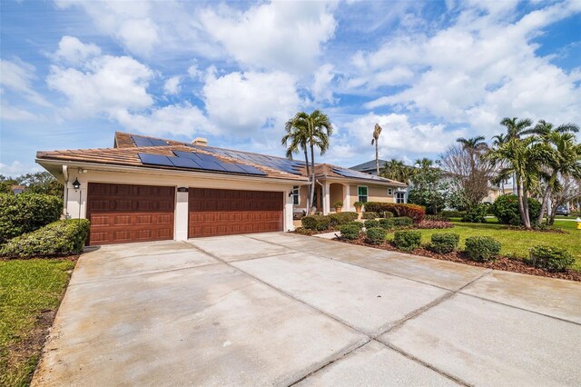 view of front facade with stucco siding, solar panels, concrete driveway, a front yard, and a garage