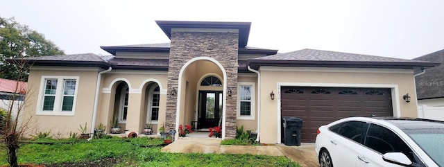 view of front of property with an attached garage, stone siding, roof with shingles, and stucco siding