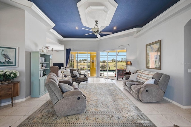 living room featuring a tray ceiling, light tile patterned flooring, a ceiling fan, and baseboards