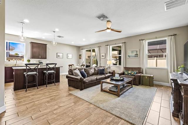 living area with light wood-style floors, visible vents, a textured ceiling, and baseboards