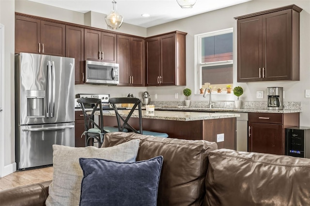 kitchen with dark brown cabinetry, light stone counters, open floor plan, stainless steel appliances, and light wood-type flooring