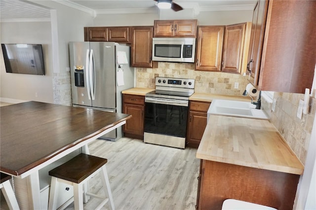 kitchen featuring stainless steel appliances, a sink, ornamental molding, light wood-type flooring, and tasteful backsplash