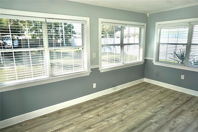 empty room featuring a wealth of natural light, crown molding, a textured ceiling, and wood finished floors