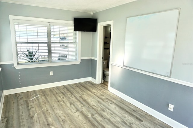 empty room featuring crown molding, wood finished floors, and baseboards