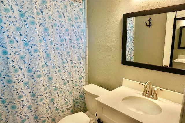 bathroom with a textured wall, curtained shower, vanity, and toilet