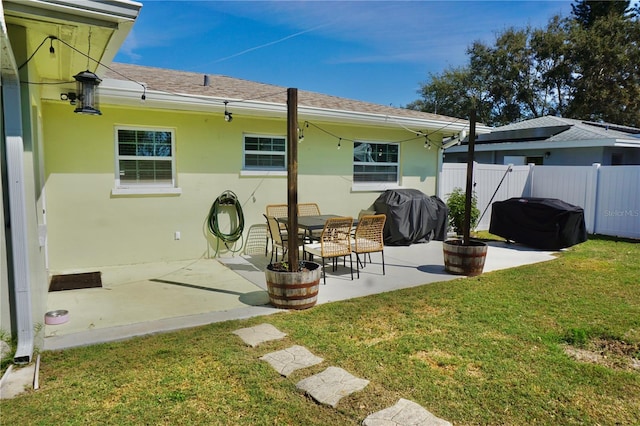 rear view of property with a shingled roof, fence, a yard, a patio area, and stucco siding