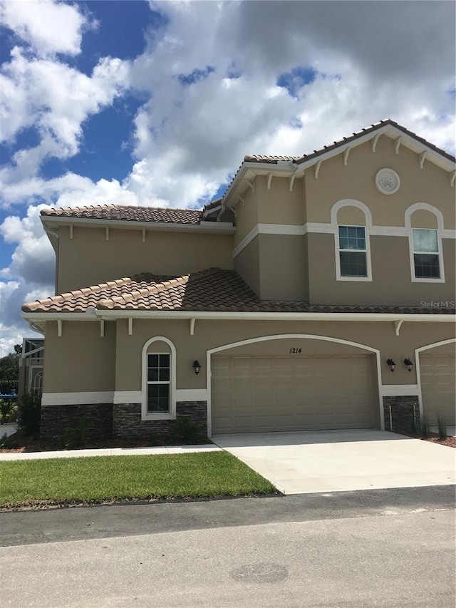 view of front of property with driveway, stone siding, a tile roof, and stucco siding