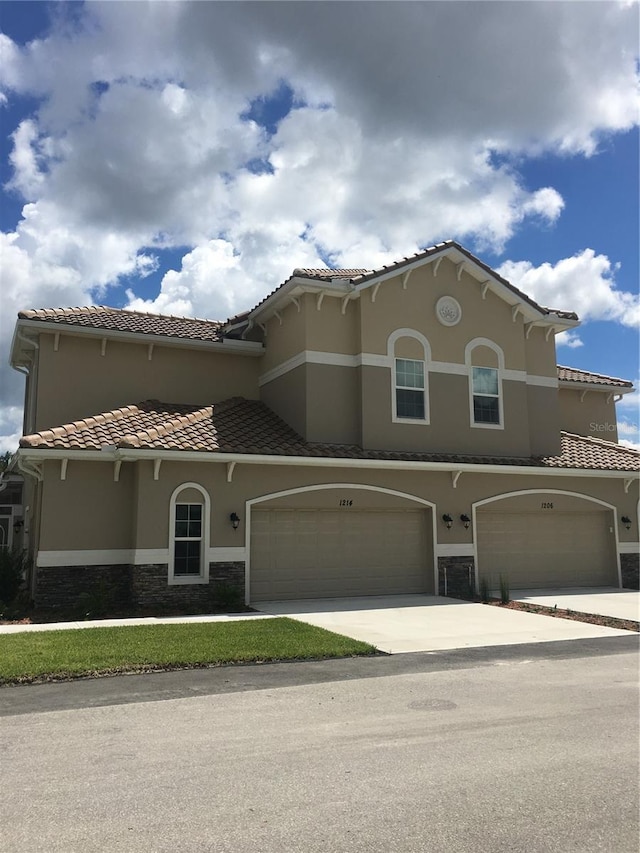 mediterranean / spanish house featuring a garage, stone siding, a tiled roof, driveway, and stucco siding