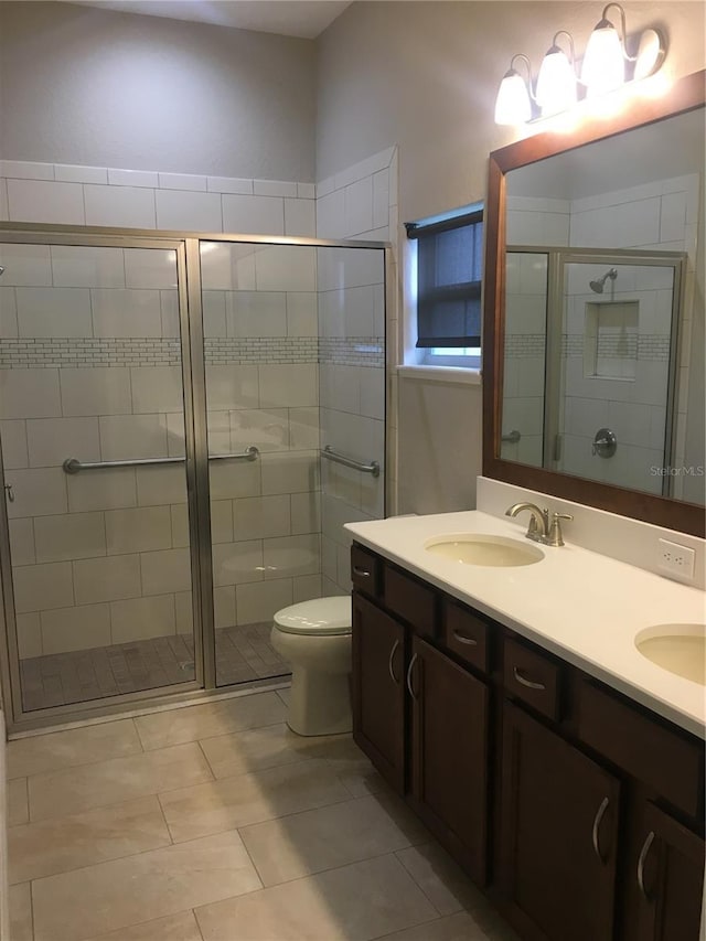 bathroom featuring double vanity, toilet, tile patterned floors, a shower stall, and a sink