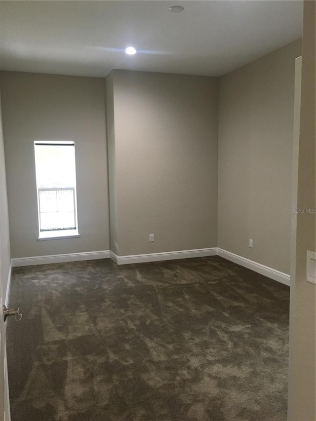 unfurnished room with dark carpet and baseboards