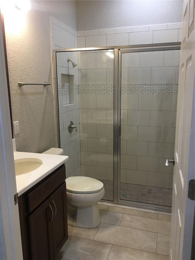 bathroom featuring a textured wall, a stall shower, and vanity