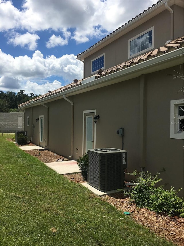 view of side of home with central AC, a yard, a tiled roof, and stucco siding