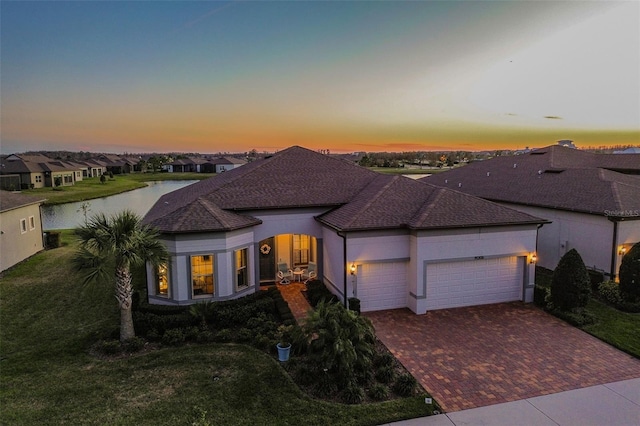 view of front facade featuring a shingled roof, an attached garage, a water view, decorative driveway, and a front yard