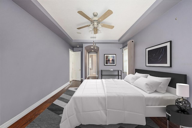 bedroom with dark wood-type flooring, a ceiling fan, baseboards, and ensuite bathroom