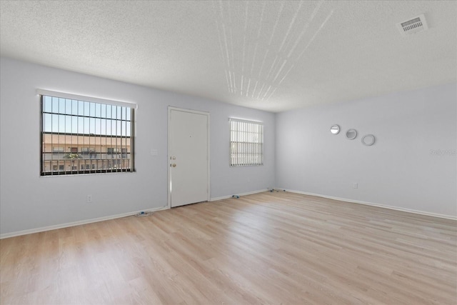 spare room featuring baseboards, light wood-style flooring, visible vents, and a textured ceiling